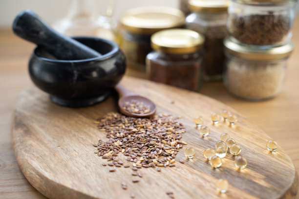 横放照片:一个装满亚麻籽的木勺，旁边是一个装着亚麻油和一束亚麻植物的小玻璃瓶图片下载