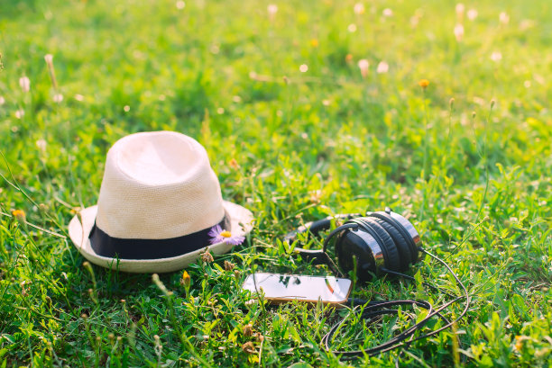 待在公园里。日落时分，在绿油油的草地上戴上帽子、耳机和手机。图片下载