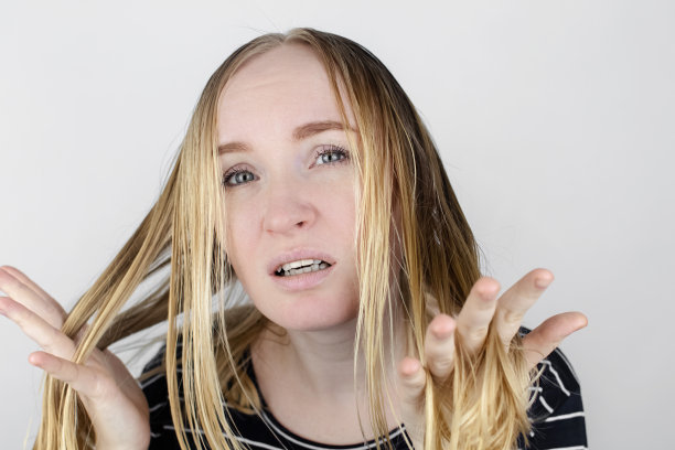 这个女孩看着镜子前她的油光发亮的头发。头皮有问题，皮脂腺分泌增多。头发护理。油性发质的护理和治疗理念图片下载