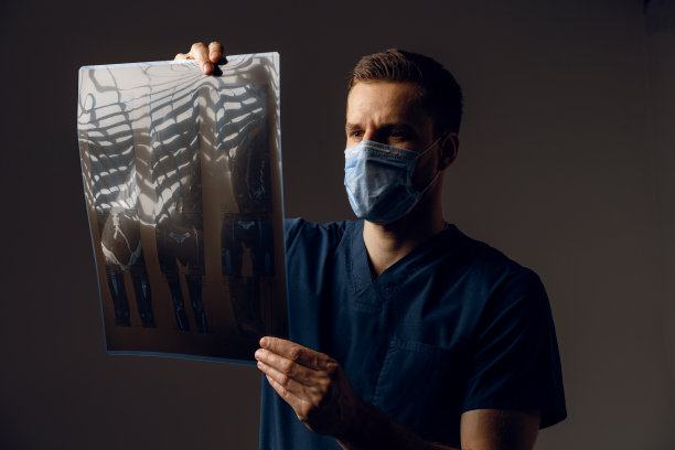 医生在医用防护口罩中拿着x光扫描病人的冠状病毒。通过电脑断层扫描。身穿医袍的外科医生在看深色背景上的扫描图。图片下载