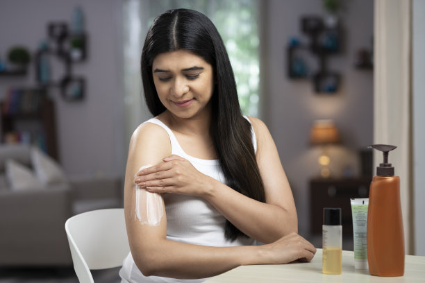 年轻女性在她的肩膀上涂抹身体乳液或水分:-库存照片图片下载