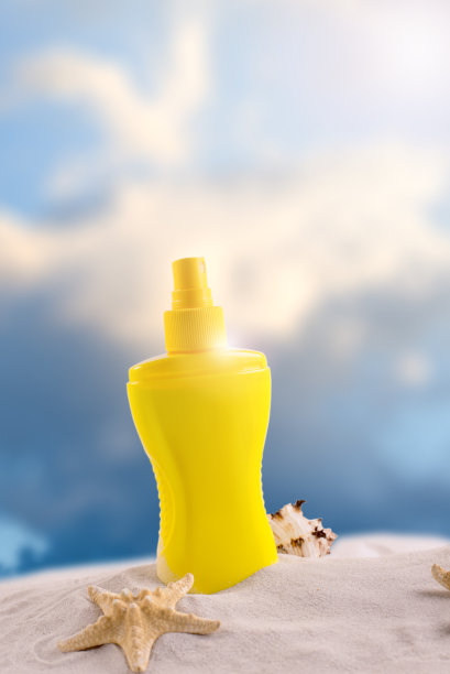 防晒喷雾瓶在沙滩上与不同的贝壳对抗海浪的背景。图片下载