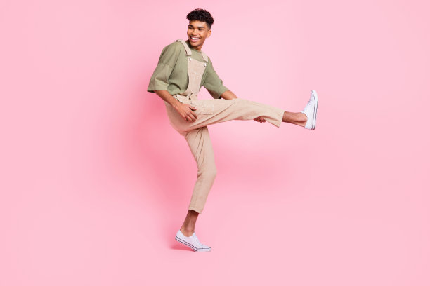 照片中的帅哥跳舞腿吉他好玩的看一边穿米色整体运动鞋孤立的粉红色背景图片下载