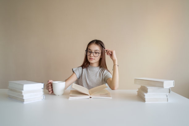 十几岁的女孩坐在桌前，拿着书做作业素材图片