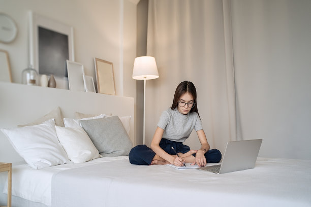 可爱的少女躺在家里的床上做作业图片下载