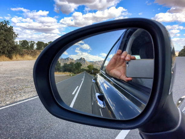 一辆汽车的后视镜上的反射，一只手拿着手机拍一张照片的反射显示出一条道路，以山景观为背景，一只手拿着手机图片下载