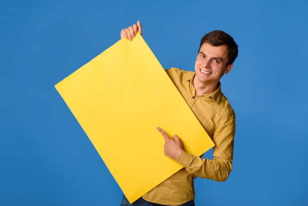 年轻的快乐的男人是拿着一个空的黄色横幅海报在蓝色的背景和笑。图片下载