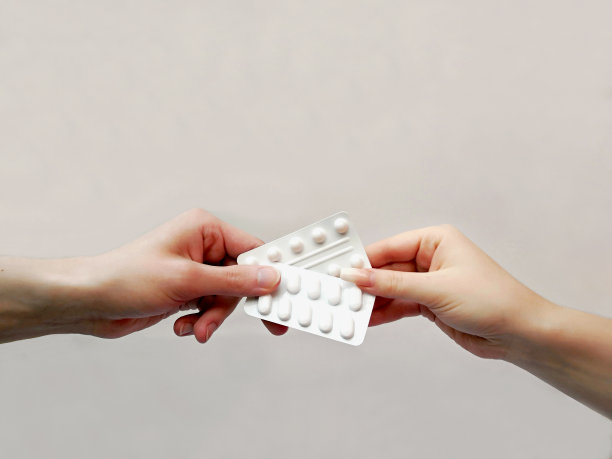 两个人的手(男人的手和剪着修长指甲的女人的手)正在搬运白色背景下装着药片的包装。医疗保健中团结的概念。在处方药物图片下载