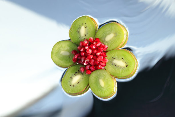 切片成熟的猕猴桃片和石榴石特写形式的花。模糊的蓝色背景上的热带水果。糖，果冻，果酱。健康食品.vegans。文本。图片下载