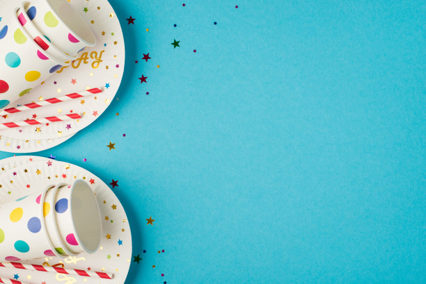 俯视图照片的生日表组成与亮片纸杯和吸管在两个盘子上孤立的蓝色背景与copyspace在右边图片下载