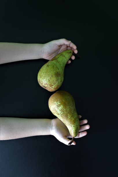 在黑色的背景上，两只手拿着两个梨图片下载