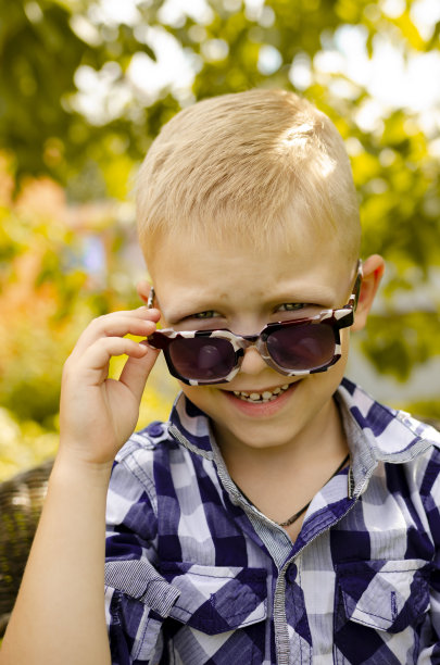 男孩戴上了太阳镜。把你的手放在太阳镜上。在阳光下眯着眼图片下载