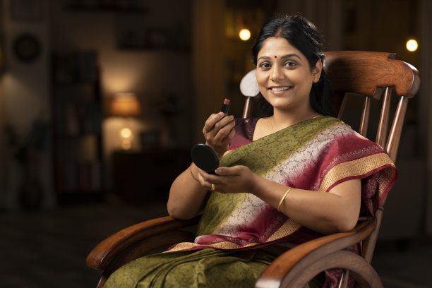 一个穿着纱丽的女人坐在家里的摇椅上涂口红的照片:-股票照片图片下载