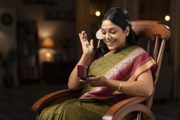 一个穿着纱丽的女人坐在家里的摇椅上打开戒指的钻石盒子时被震惊了:-股票照片图片下载