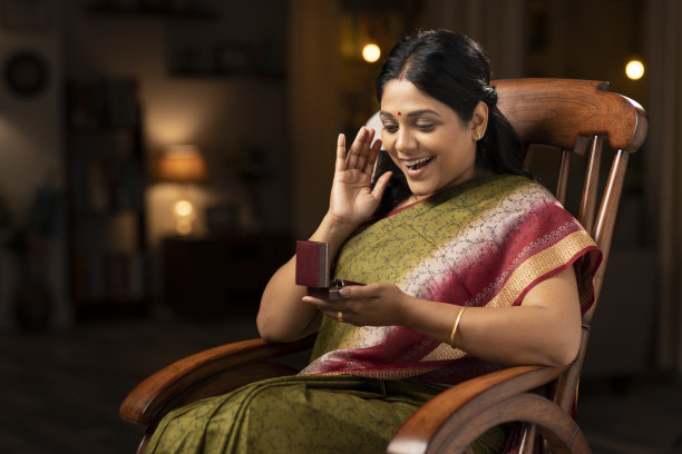 一个穿着纱丽的女人坐在家里的摇椅上打开戒指的钻石盒子时被震惊了:-股票照片图片下载