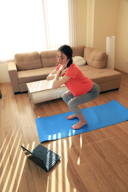 年轻女子做运动在家里与互联网的帮助图片下载
