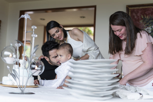 整个家庭在客厅享受洗礼派对，他们装饰好了放蛋糕的桌子，受洗的婴儿看着照片中的摄像机图片下载
