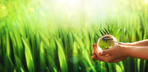 双手捧着玻璃绿色星球在阳光灿烂的背景。环境概念世界地球日横幅。拯救地球。图片下载