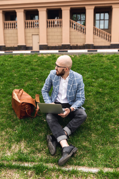 时尚男士坐在草坪上用笔记本电脑工作。自由职业者,博主。现代人的生活图片下载