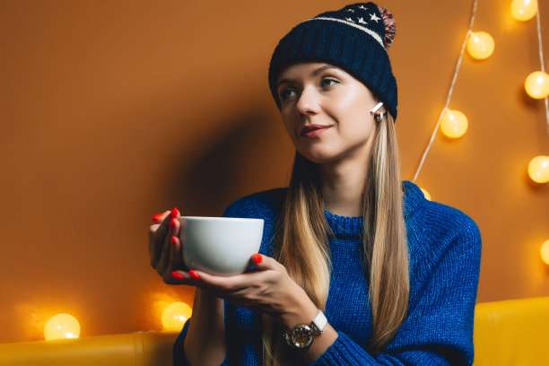 年轻女子正在室内喝咖啡。女人像一杯热饮。女孩正在用白色无线耳机打电话。自由的概念图片下载