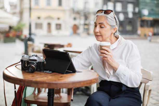成熟的女士喝咖啡和使用平板电脑在咖啡馆露台图片下载