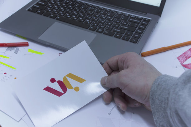 创意工作场所的平面设计师。办公室里的一个男人正在桌子上开发一个标志，背景是打印的草图和一台笔记本电脑。图片下载