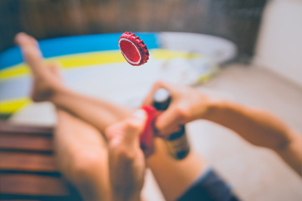 用打火机开一瓶啤酒。把注意力放在空中的帽子上。喝冰啤，享受阳光明媚的夏日周末图片下载