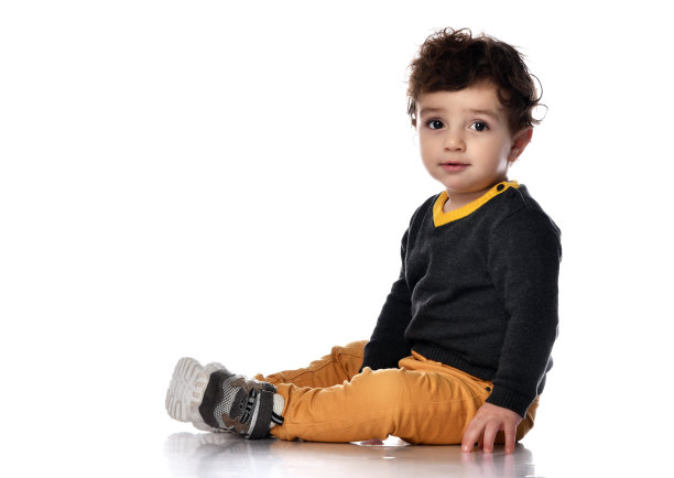 穿着黄色裤子的婴儿斜坐在地板上看着我们，背景是白色的，有自由文本的空间图片下载