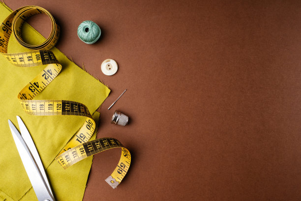 织物和缝纫工具的针线活在一个棕色的背景，平，平，俯视图，复制空间。创造时尚服装理念。水平背景广告或包装图片下载