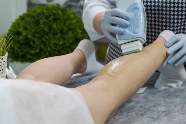 美容和医疗保健。一个美容师做脱毛与热蜡在女人的腿上使用蜡装置在水疗中心的特写。水平的作文图片下载