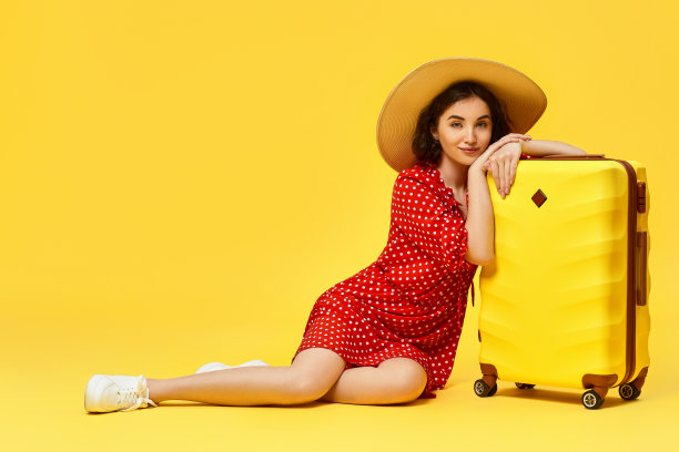 黄色背景下提着行李箱旅行的女人。图片下载