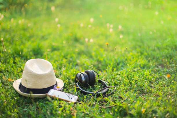 待在公园里。日落时分，在绿油油的草地上戴上帽子、耳机和手机。图片下载