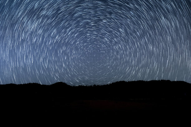 夜晚美丽的螺旋星迹。奇异的星星是与山的背景延时，星星的轨迹在多彩的夜空与剪影的地平线在前景。图片下载