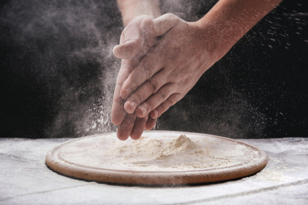 一个男厨师在黑色的背景上拍着他装满白面粉的手。自制烘焙工艺，烘焙理念。图片下载