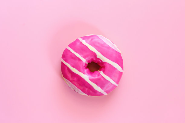 美味的草莓甜甜圈。自制的粉色糖霜和白色条纹的圆形甜甜圈，在时尚的软粉色背景位于图像的中心。油炸圈饼糕点。图片下载
