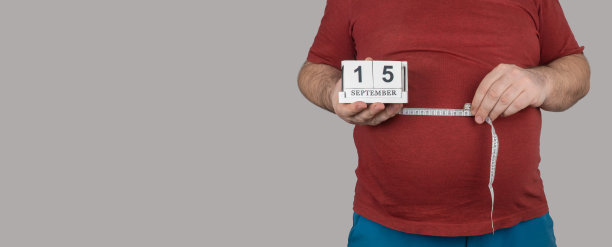 胖子用一厘米的卷尺测量腹部的大小。9月15日，减肥日。人们饱受超重之苦。横幅,复制空间图片下载