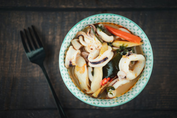 鲜嫩的海鲜鱿鱼在一碗冬阴功汤中，以木色为背景，直接摆在上面。图片下载