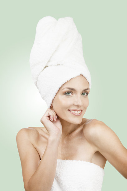 年轻的女孩卷毛巾在她的头在绿色的背景。美学的概念。图片下载