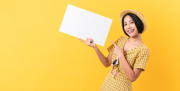 年轻的亚洲妇女拿着空白纸，微笑着看着橙色的背景。广告的迹象。图片下载