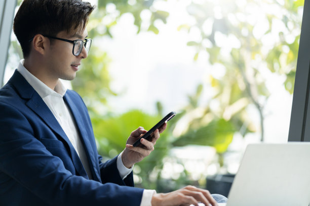 创意机构智能眼镜亚洲男性正式服装对话智能手机自由职业者工作与笔记本电脑在共同工作区域办公空间与模糊的办公室背景清新图片下载