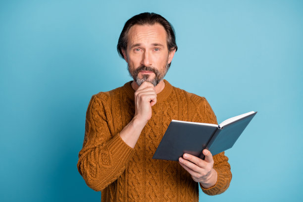 照片肖像的男人聪明的触摸下巴，深思的看书老师孤立在明亮的蓝色背景图片下载