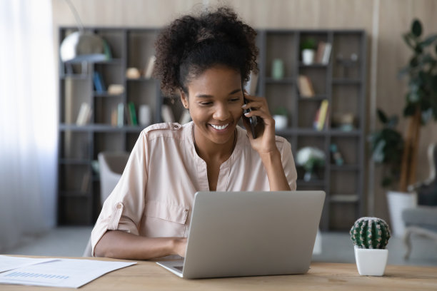 微笑的混血儿女人在笔记本电脑上工作在智能手机上聊天图片下载