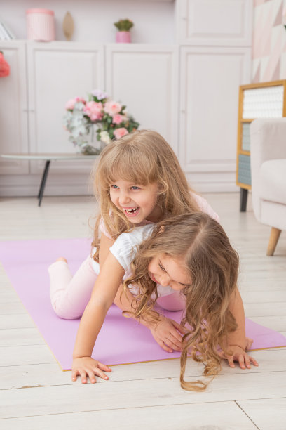 一对小女孩在客厅里微笑着在瑜伽垫上玩耍的垂直照片，健康的生活习惯和生活理念。图片下载