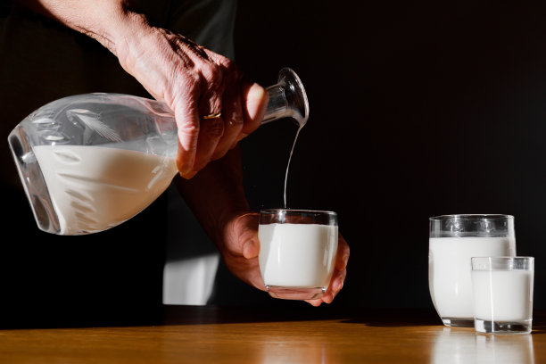 男子将新鲜牛奶倒进木桌上的玻璃杯里图片下载