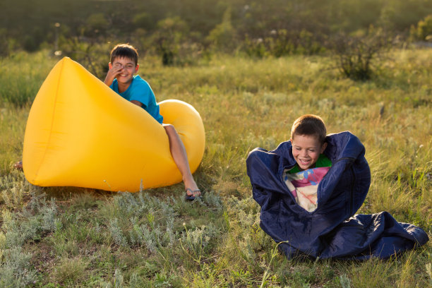 两个男孩在大自然中玩得很开心，一个坐在lamzak上，另一个在睡袋里，一个有趣的早晨图片下载