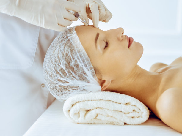 美丽的女人接受美容注射与闭上眼睛在医疗中心。美容师医生用注射器给女性脸部做美容手术图片下载