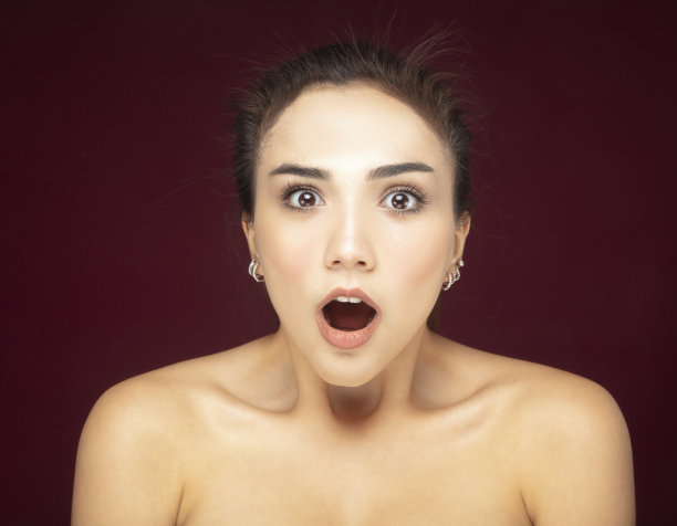 红色背景下惊讶的年轻女子的肖像。图片下载