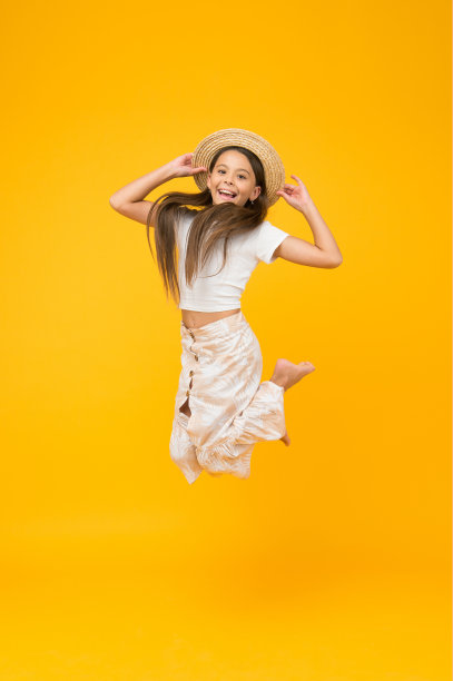 超级活跃的孩子跳草帽。光着脚的孩子感到自由。充满了幸福。夏天孩子时尚。小女孩在黄色的背景上跳得很高。精力充沛的孩子在度假图片下载