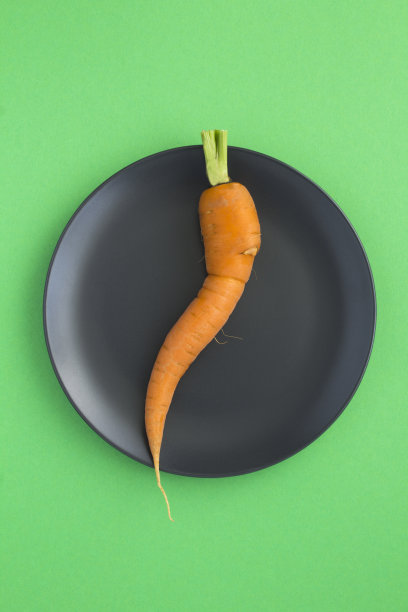 丑陋的食物。胡萝卜在黑色盘子里，在绿色背景的中央。特写镜头。图片下载