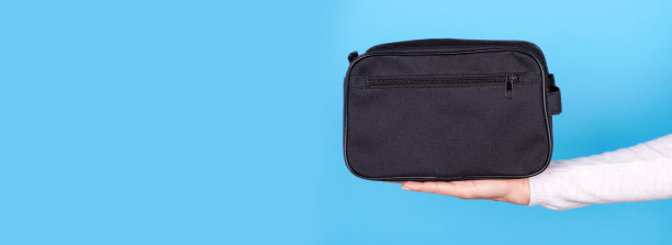 手拿黑色化妆包在蓝色的背景。图片下载